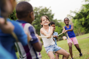 School children playing tug of war with rope in park