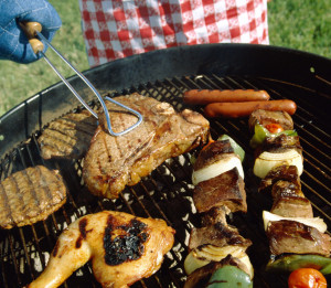 Man using tongs on meat cooking in a barbecue grill