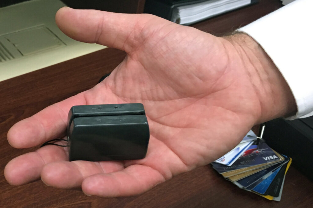 Hand holding credit card skimmer device.