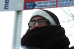 A man waits in the cold weather for a bus to arrive.