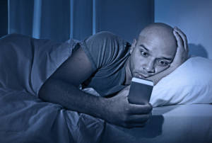 Young cell phone addict man in bed using smartphone