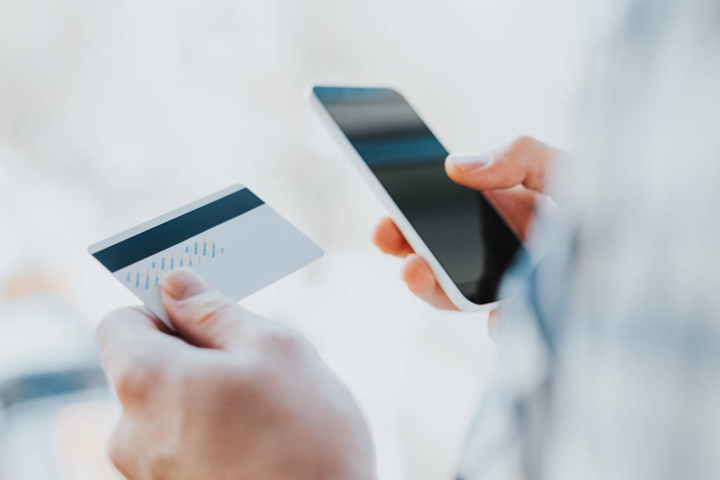 Young man hands holding credit card and using phone