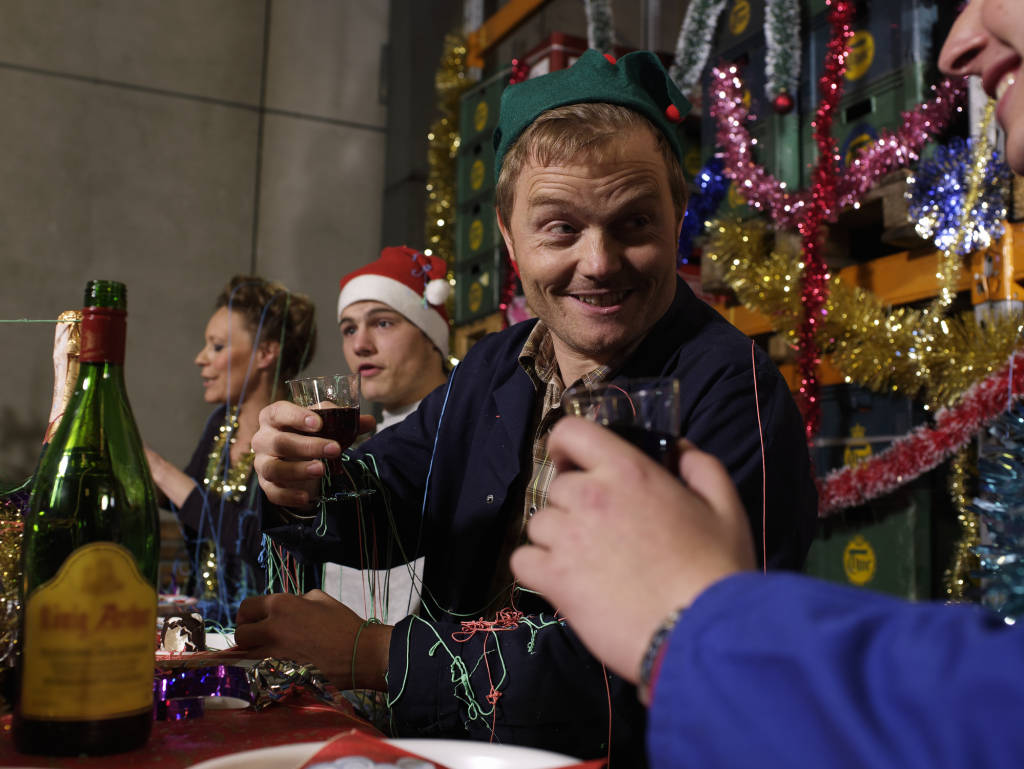 Group of workers sitting at christmas table in warehouse holding wine glasses