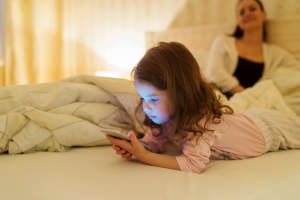 Little girl with smartphone lying in a bed, bedtime