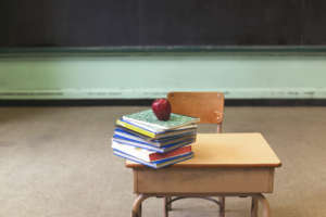 Stack of school books and apple on desk in empty classroom