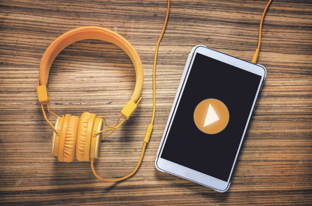 Play button on tablet with headphones on wooden table