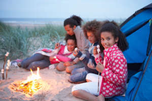 Several people outside of a tent gathered around a fire