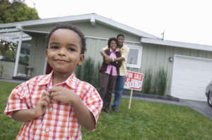 Portrait of boy (5 6) in front of new house, parents in background