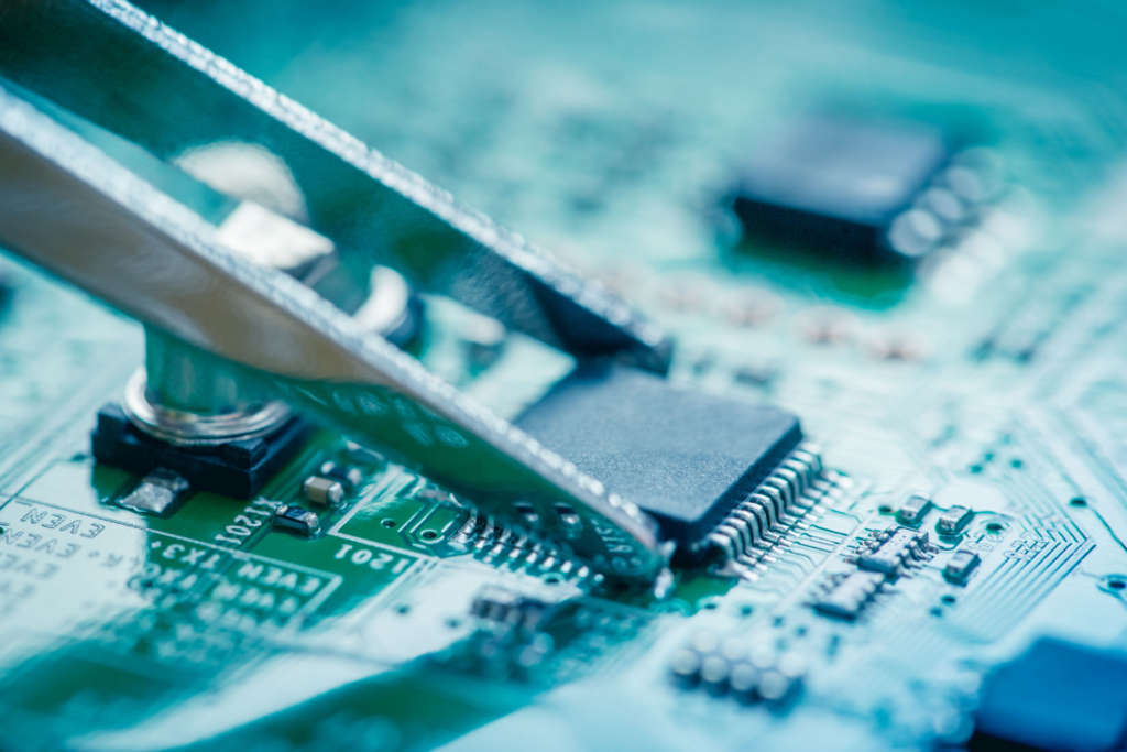 Close up on microchip catching with tweezers on circuit board.