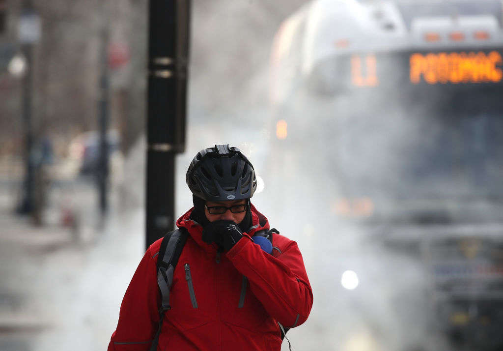A man bundled up as he walks past a steam grate.