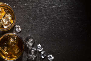 Glasses of whiskey with ice on black stone table