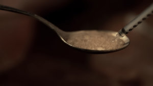 Syringe withdrawing heroin boiling on spoon, substance dependence, close up