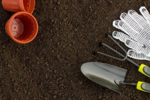 Top view of gardening tools, flower pots and textile gloves on brown soil background copy space
