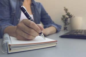 Woman's hands with pen writing on notebook. Modern grey office desk. Working, writing concept