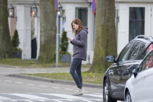 Young woman looks at her cellphone and does not pay attention to traffic