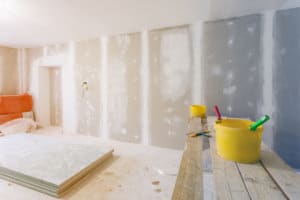 Putty knife, yellow buckets with glue and glue rollers on the wooden board in room is under construction, remodeling, renovation, extension, restoration and reconstruction.