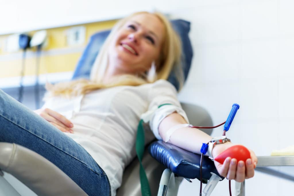 Young caucasian woman with toy heart in the hand donates blood for saving lives and medical research