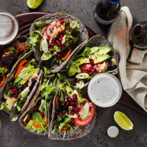 Gluten free vegan tacos from black bean with tomato and avocado salad with tahini sauce and pomegranate seeds. healthy fast food for the whole family or party on a dark background with beer
