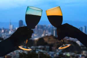 Hands of female's and male's with glass of wine on San Francisco city background.