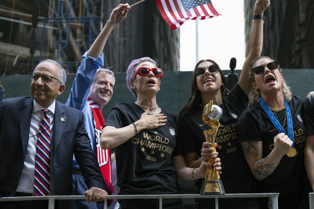 From left, U.S. Soccer Federation President Carlos Cordeiro, New York Mayor Bill de Blasio and U.S. women's soccer players Megan Rapinoe and Alex Morgan joins teammates and others as the U.S. women's soccer team is celebrated with a ticker tape parade along the Canyon of Heroes, Wednesday, July 10, 2019, in New York. The U.S. national team beat the Netherlands 2-0 to capture a record fourth Women's World Cup title. Player at right is unidentified. (AP Photo/Craig Ruttle)