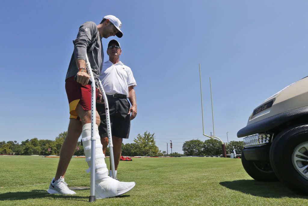 Injured Washington Redskins quarterback Alex Smith, left, walks to a cart as he talks with former quarterback Joe Theisman, right, as he leaves the practice field during the first day of NFL football training camp in Richmond, Va., Thursday, July 25, 2019.
