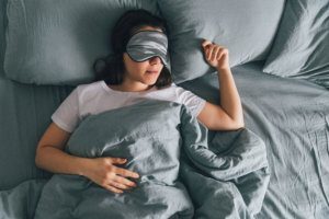 Woman sleep in eye patch in grey bed. copy space