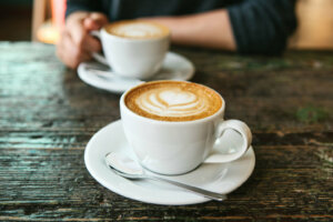 Two cups of coffee on a wooden table, the girl holds in her hand one cup of coffee in the background. A photo indicates a meeting of people and a joint pastime.