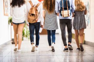Unrecognizable teenage students in high school hall.
