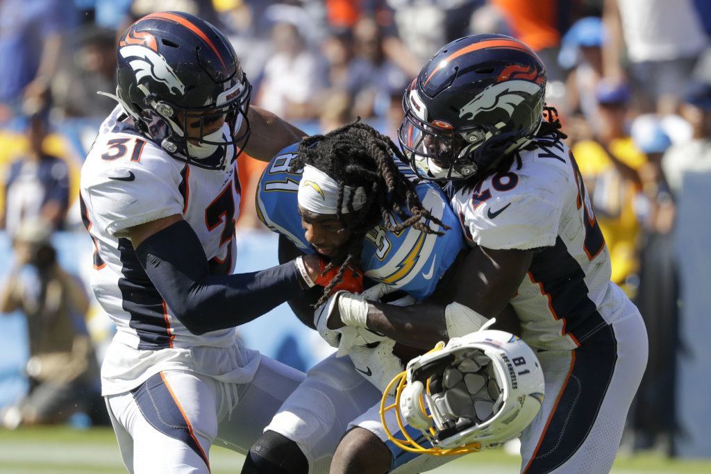 Denver Broncos free safety Justin Simmons, left, and cornerback Isaac Yiadom, right, tackle Los Angeles Chargers wide receiver Mike Williams as he looses his helmet during the first half of an NFL football game Sunday, Oct. 6, 2019, in Carson, Calif.