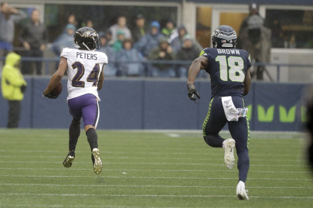Baltimore Ravens cornerback Marcus Peters (24) runs for a touchdown after he intercepted a pass intended for Seattle Seahawks wide receiver Jaron Brown (18) during the first half of an NFL football game, Sunday, Oct. 20, 2019, in Seattle.