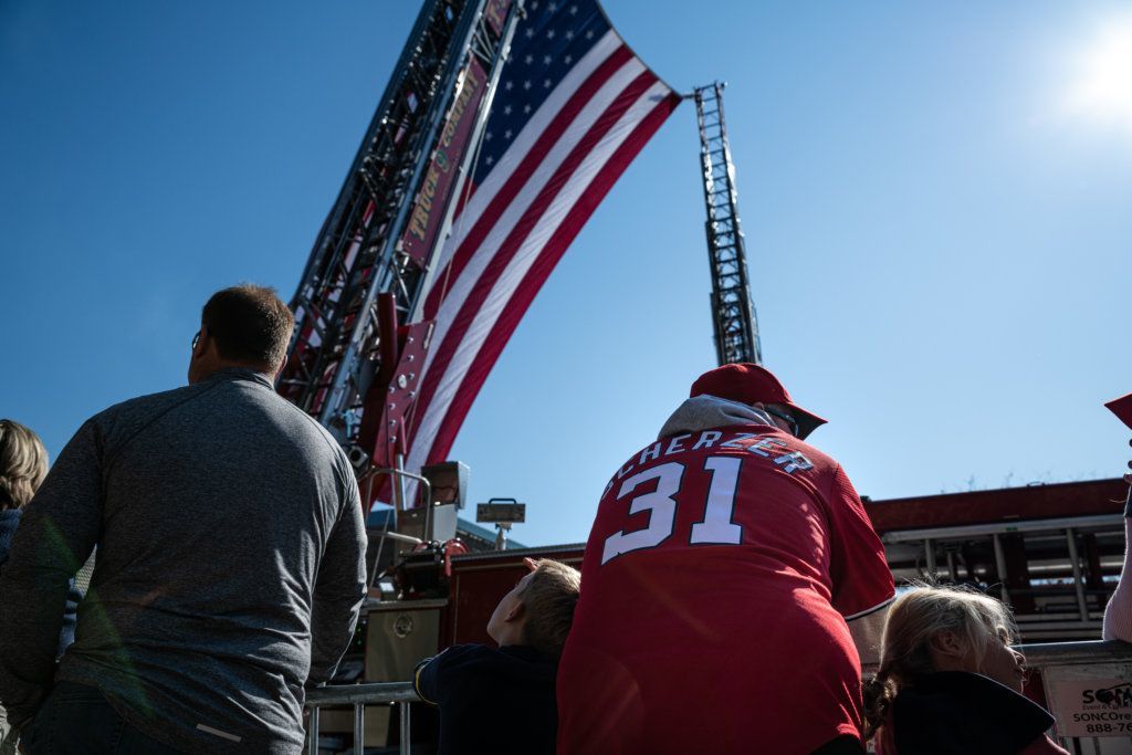 A Washington Nationals fan awaits the start of the parade, beneath an American flag hoisted by two D.C. fire engines.