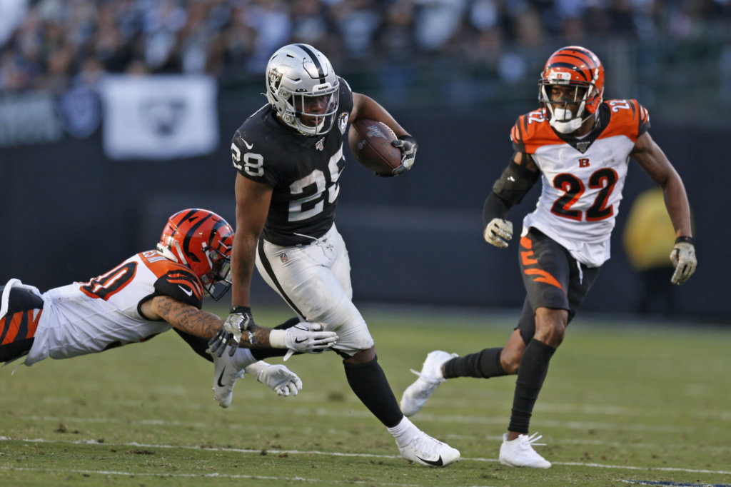 Oakland Raiders running back Josh Jacobs runs with the ball away from Cincinnati Bengals free safety Jessie Bates as Bengals cornerback William Jackson (22) looks on during the second half of an NFL football game in Oakland, Calif., Sunday, Nov. 17, 2019.
