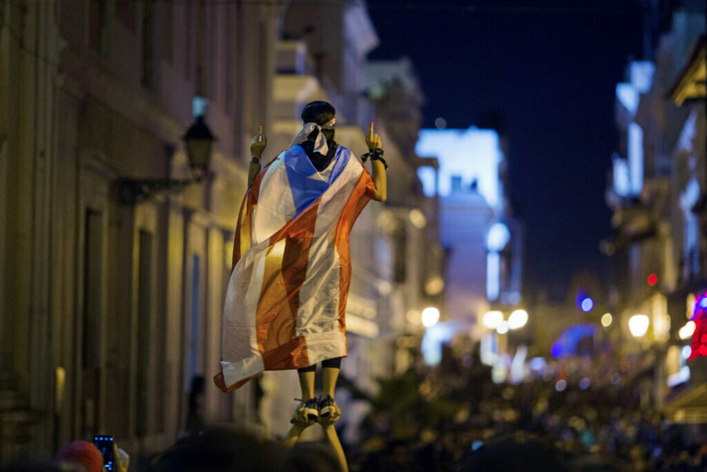 A demonstrator wearing a Puerto Rican flag joins thousands of others in a march to the governor's residence in San Juan, Puerto Rico, on July 17, 2019. The protesters chanted demands for Gov. Ricardo Rossello to resign after the leak of online chats that showed him making misogynistic slurs and mocking his constituents.