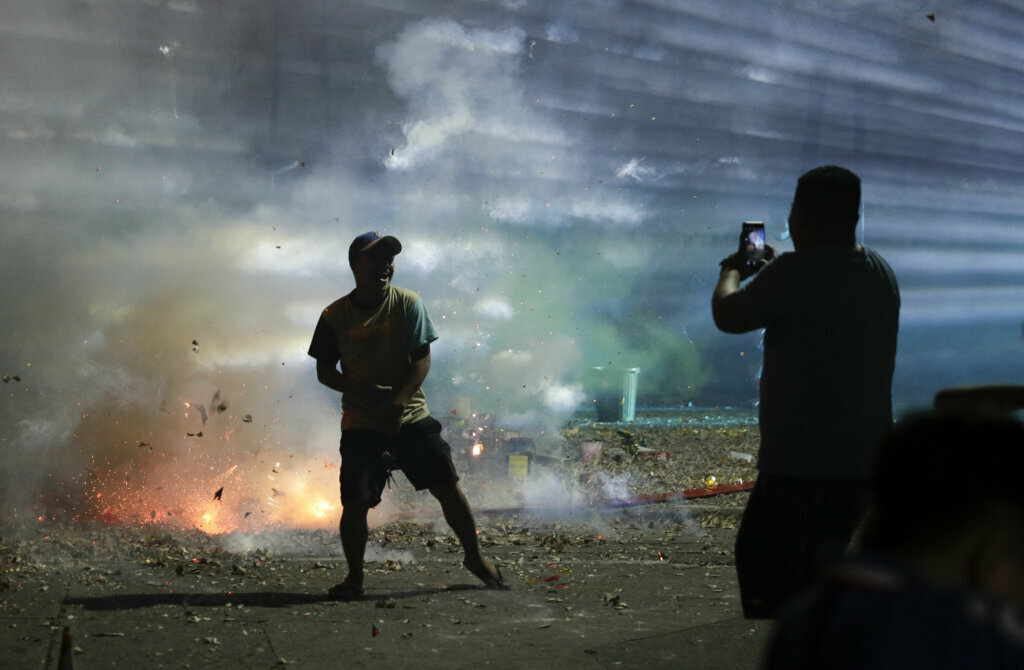 A person poses for a selfie beside exploding firecrackers as they celebrate the coming of the New Year early Wednesday, Jan. 1, 2020 in Manila, Philippines. Filipinos welcome the New Year with noise and firecrackers in the belief that this will drive away bad spirits and bring in good luck.