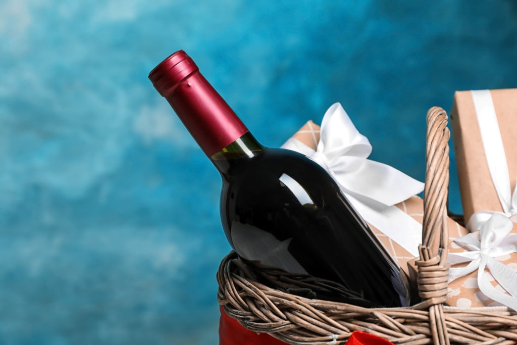 Gift basket with bottle of wine on color background