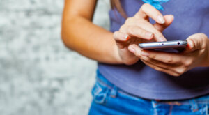 Young teenager girl hand using mobile phone or smartphone on gray wall background