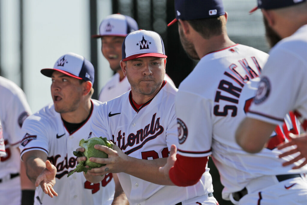Washington Nationals' JB Shuck, center, is handed a cabbage by teammate Javy Guerra, left, before handing it to Hunter Strickland, right, as part of a team building exercise during spring training baseball practice Monday, Feb. 17, 2020, in West Palm Beach, Fla. The event was also held to mark National Cabbage Day.