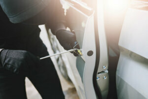 Close up hand pulling the handle of a car thief wearing black clothes and glove stealing automobile trying door handle to see if vehicle is unlocked trying to break into. car theft concept.