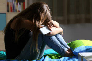 Sad teen with a phone in her bedroom