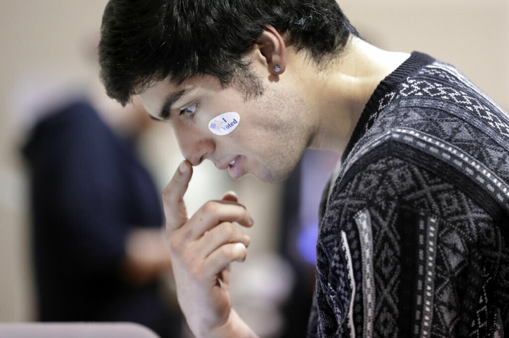 David Flores-Figueroa wears his voting sticker on his face as he reads over the ballot before voting on Super Tuesday at the Cleveland Park Community Center precinct, Tuesday, March 3, 2020, in Nashville, Tenn. Deadly overnight tornadoes delayed the start of the presidential primary voting in Nashville and another Tennessee county, spurring elections officials to redirect voters from some polling places to alternate locations. Voters from six precincts were combined to vote at Cleveland Park, where the wait could take up to an hour or more.