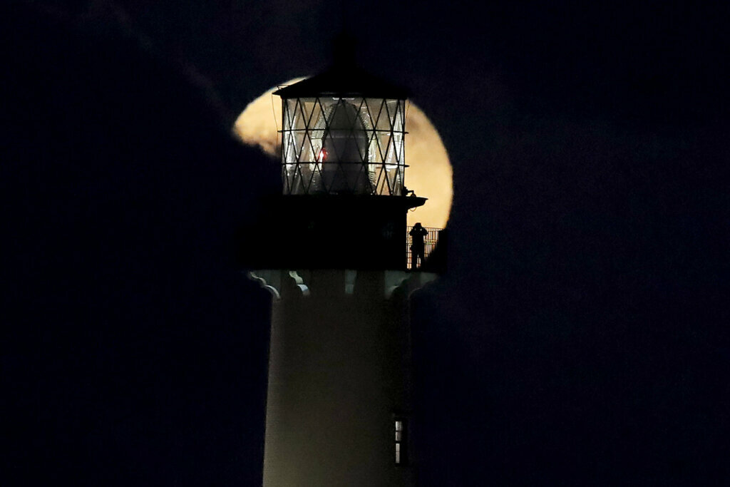 A person standing on the platform of the Jupiter Lighthouse looks at the supermoon as it is partially obscured by a cloud, Monday, March 9, 2020, in Jupiter, Fla. The 108-foot, brick lighthouse was first lit in 1860.