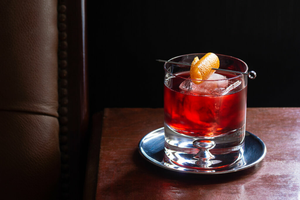 Negroni Cocktail, with Gin, Red Vermouth, and Campari, over Ice with Orange Twist in Dark Luxurious Bar