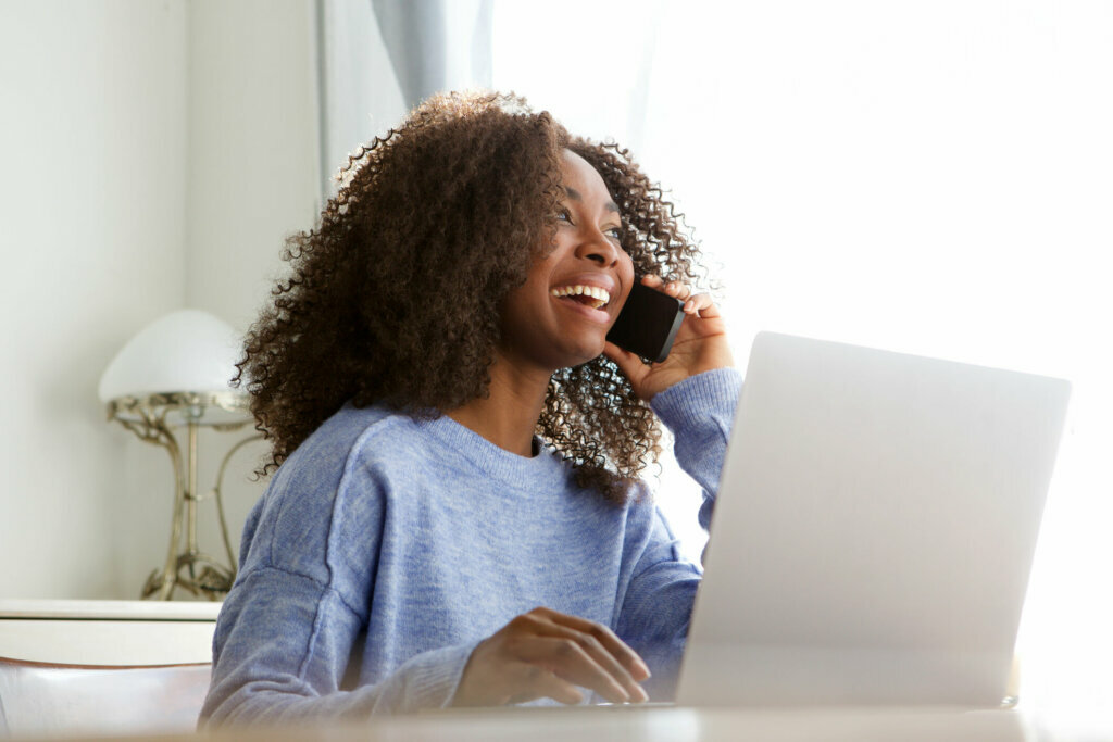 Laughing young woman sitting at table with laptop talking and mobile phone