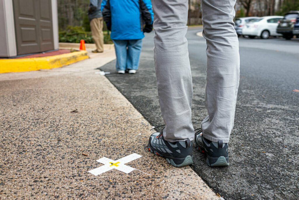 People standing waiting in line far apart to maintain social distance distancing during covid 19 coronavirus outbreak with mark cross signs on sidewalk pavement by grocery food store shop shopping
