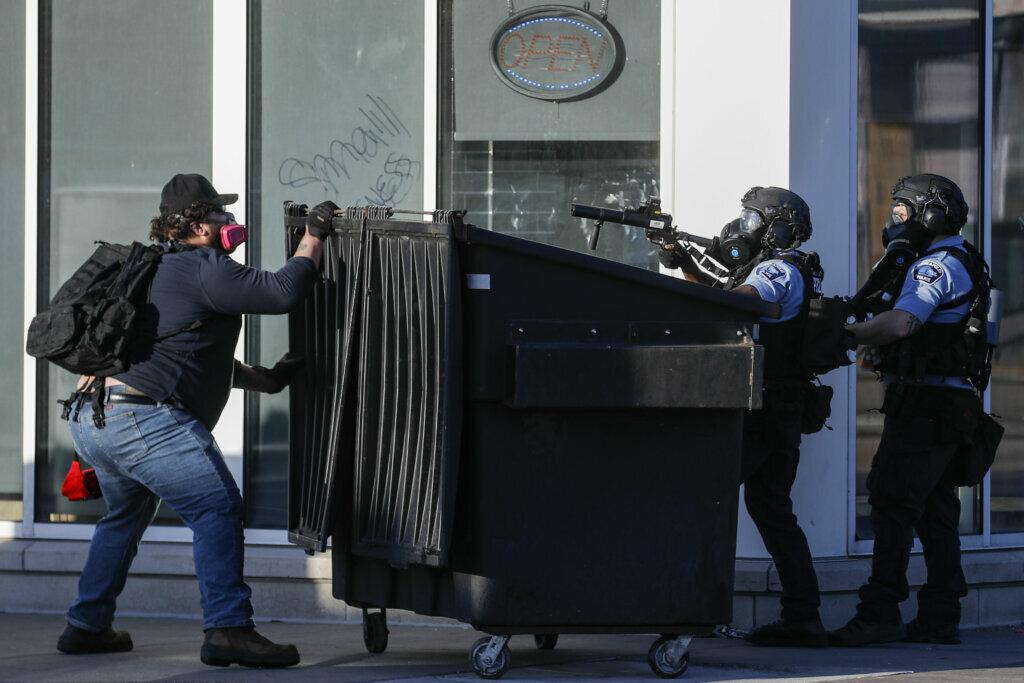 A protester faces off with two police officers using less-lethal ammunition in their weapons, Thursday, May 28, 2020, in St. Paul, Minn. Protests over the death of George Floyd, a black man who died in police custody Monday, broke out in Minneapolis for a third straight night. (AP Photo/John Minchillo)