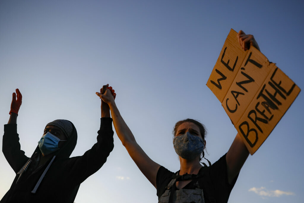 Protesters demonstrate on University Avenue while holding a "WE CAN'T BREATHE" sign and wearing protective masks, Thursday, May 28, 2020, in St. Paul, Minn. Protests over the death of George Floyd, a black man who died in police custody Monday, broke out in Minneapolis for a third straight night. (AP Photo/John Minchillo)
