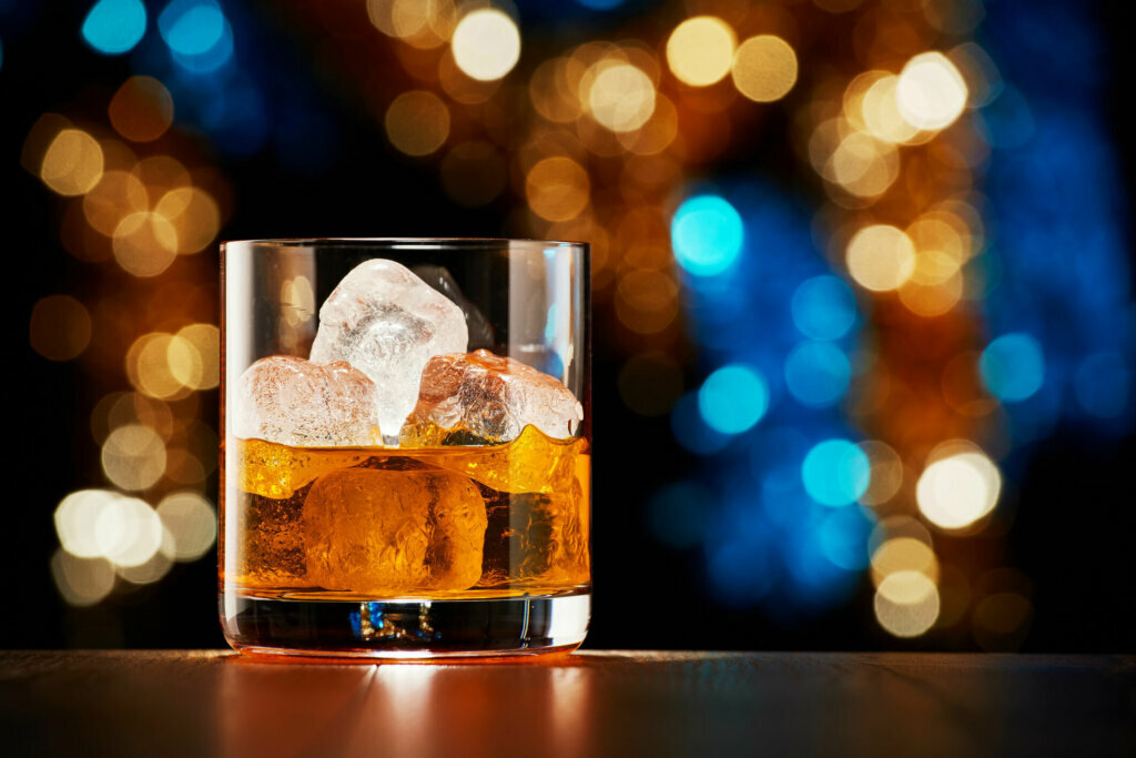 Glass of whiskey with ice on colorful Christmas lights bokeh background