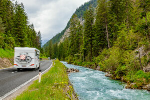 Camper van with attached bicycle driving through the European Alps on a rainy day