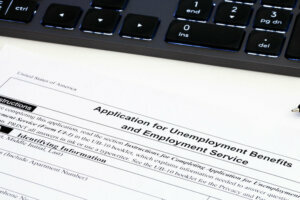 Application for employment benefits form with computer keyboard and pen on white background. Unemployment rate has risen sharply in United States due to closed business caused by corona virus outbreak