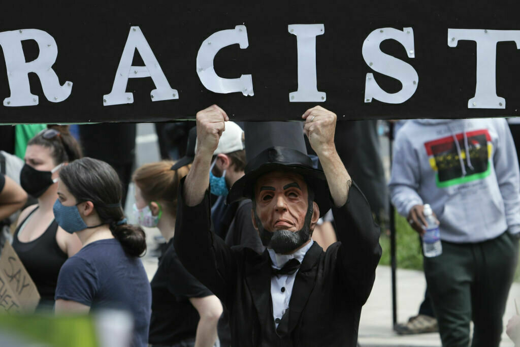A man holds a sign as he dresses as Abraham Lincoln during a protest near the Saint John Paul II National Shrine in response to the death of George Floyd while under police custody June 2, 2020 in Washington, D.C.